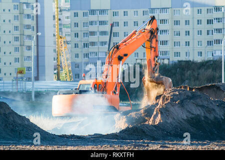 Escavatore arancione di scavare il terreno in corrispondenza del luogo di costruzione. Foto Stock