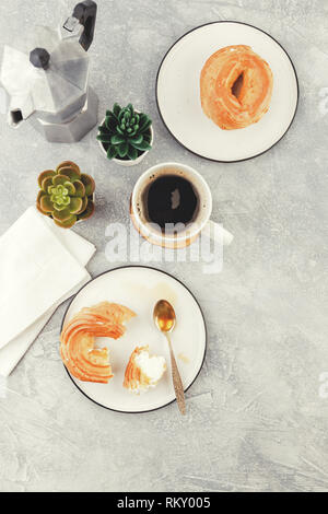 La prima colazione con soffio di crema anelli - bignè e tazza di caffè nero su uno sfondo luminoso Foto Stock