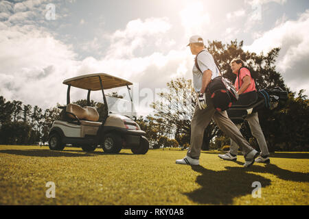 Senior golfisti camminare insieme nel campo da golf con le loro borse da golf. Senior golfisti camminare e parlare dopo il gioco. Foto Stock