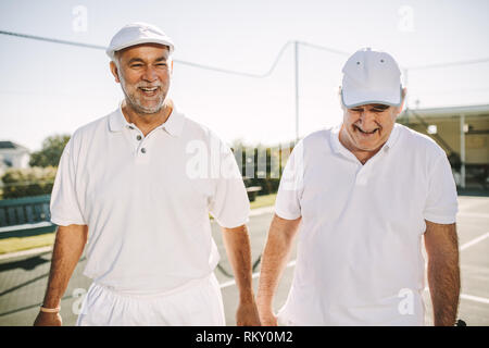 Sorridente alti uomini nel tennis usura di parlarsi camminando sul campo da tennis. Alti uomini giocare a tennis in una giornata di sole. Foto Stock