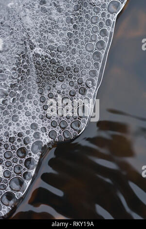 L'accumulo di bolle di aria sotto la sottile crosta di ghiaccio contro lo sfondo di un flusso turbolento dell'acqua. Foto Stock