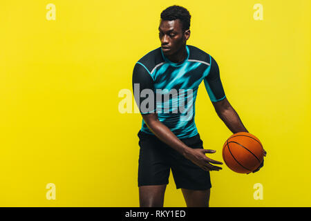 L'uomo africano giocare a basket su sfondo giallo. Sportivo praticare basket in studio. Foto Stock