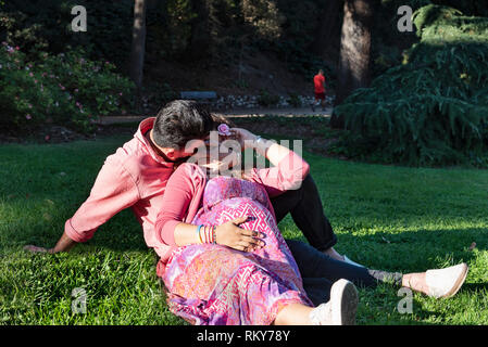 Uomo bello baciare sua moglie incinta nel parco. Il concetto di amore. Foto Stock