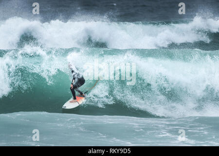 Un surfista a cavallo di un onda al Fistral Beach in Newquay in Cornovaglia. Foto Stock
