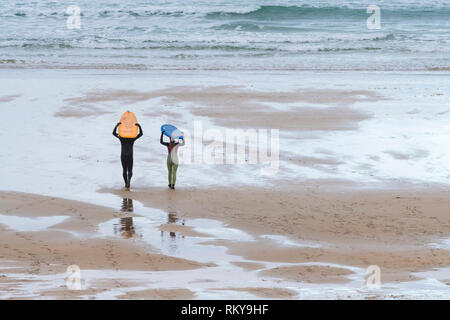 Due surfisti che trasportano le loro tavole da surf sulle loro teste e camminare fino al mare su Fistral Beach in Newquay in Cornovaglia. Foto Stock