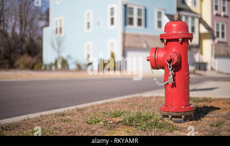 Bokeh colpo di un colore rosso brillante idrante di fuoco su una comunità di strada con una fila di case a schiera dietro di esso. Foto Stock