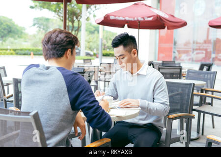Controllo delle scorte. Due business partner di lavoro sul computer che sorride allegramente su un incontro presso la caffetteria locale - Immagine Foto Stock