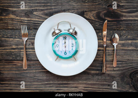 Dodici ore di digiuno intermittente e il concetto con orologio su piastra su una tavola in legno rustico / background. Vista dall'alto. Foto Stock