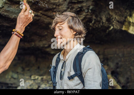 L uomo è un turista in Bali. Il rito di abluzione con acqua santa e sulla sua fronte prikleeli riso e mettere il fiore orecchio Foto Stock