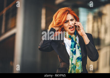 Sottolineato business donna sta parlando su smartphone nel distretto di office. Foto Stock