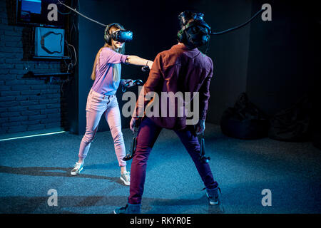 L uomo e la donna un gioco utilizzando la realtà virtuale auricolare e gamepad in camera oscura della riproduzione di club Foto Stock