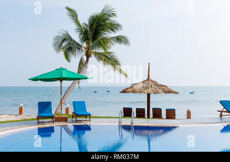 Sedie reclinabili e sfumature sotto le palme attorno a una piscina all'aperto Foto Stock