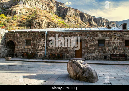 Nel cortile del Monastero di Geghard di Armenia con la pietra santa e panchine per i pellegrini presso i locali per per i sacerdoti Foto Stock