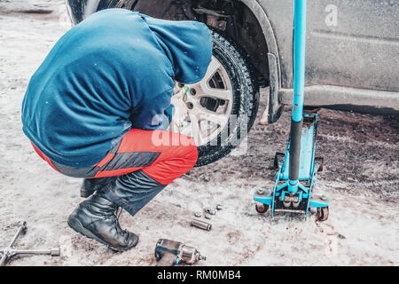 Il processo di lavoro di rimozione delle ruote dalla macchina sulla strada in inverno. Sostituzione di pneumatici invernali per l'estate. Foto Stock