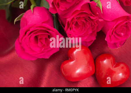 Primo piano della red due cuori e bouquet di rose, sul tessuto rosso sfondo. Foto Stock