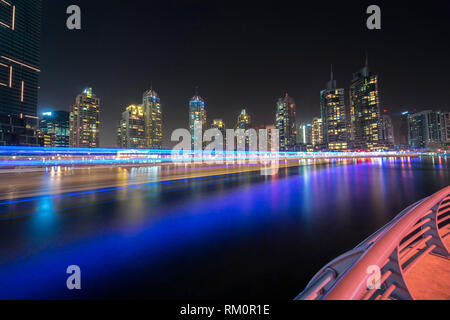 Un illuminato tradizionale dhow Arabo appare come se è in movimento a velocità di ordito lungo le acque luccicanti del porticciolo turistico di Dubai. Foto Stock