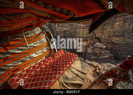 Le colorate coperte e cuscini di cliffside tenda beduina telaio la facciata del famoso tesoro di Al Khazneh. Foto Stock