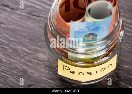 Vaso di vetro con le monete e le banconote in euro su un tavoli in legno nero con una iscrizione PENSIONE. Concetto di risparmi finanziari per ricchi di vecchiaia Foto Stock