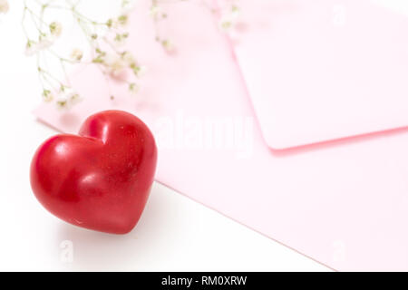 Primo piano di un cuore rosso con busta rosa e fiori bianchi. Foto Stock