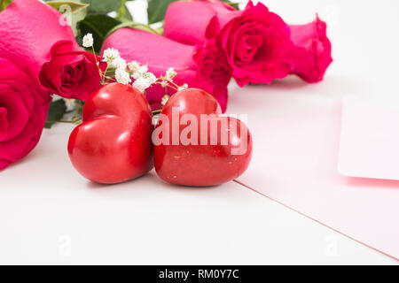Due cuori rossi con busta rosa e rose rosse closeup. Foto Stock