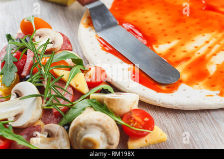 La cottura della pizza. Applicazione di salsa di pomodoro sulla pasta Foto Stock