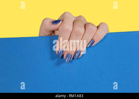 Primo piano vista superiore della femmina bianca con mano lucida brillante blu moderno gel polish. Macro di curato di chiodi di donna adulta isolati su giallo e blu di ba Foto Stock