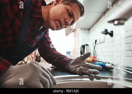 Vista interna. Close-up di bello plumber riparazione lavello in cucina. Foto di metalic lavandino e tuttofare con cacciavite Foto Stock