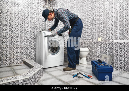 Il controllo della macchina di lavaggio di lavoro. Uomo di lavoro idraulico in bagno il lavoro di test di wacher mashine vicino a cassetta portautensili Foto Stock