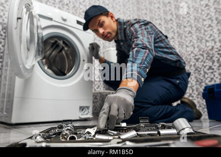 Cose necessarie sono sempre a portata di mano. Uomo di lavoro idraulico in bagno sfocato vicino alla macchina di lavaggio. Uomo di lavoro idraulico in bagno il controllo del lavoro di wacher mashine di close-up Foto Stock