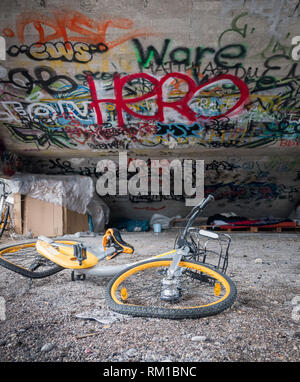 Vecchio rottame giallo biciclette sotto il cemento scale con graffiti e senzatetto rifugio del sonno Foto Stock