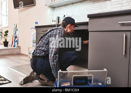Controllare eventuali problemi. Giovani tuttofare riparazione lavandino in cucina Foto Stock