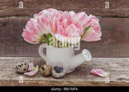 Molla della scheda Messaggi di saluto. Le uova di pasqua rosa tulipani freschi bouquet di fiori piccoli toy annaffiatoio vaso a rustico in legno squallido sfondo. Concetto di pasqua. Cop Foto Stock
