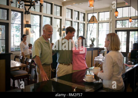 Senior essendo donna affettuosa verso il suo nipote adolescente come suo marito gli ordini un caffè in un bar. Foto Stock