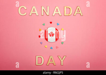 Happy Canada Day greeting card con lettere in legno. Parole e bandiera canadese con molte caramelle cuori attorno ad esso su coralli viventi sfondo rosa. Multic Foto Stock