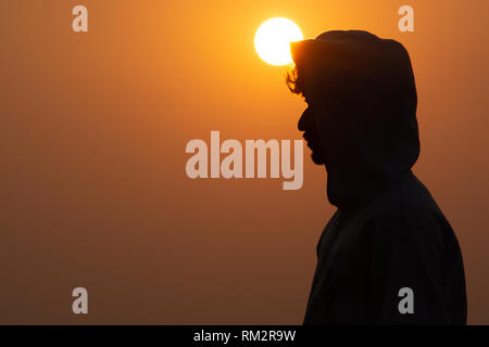 In prossimità di una persona stancato felpa con cappuccio in piedi sopra la montagna con sfondo al tramonto Foto Stock