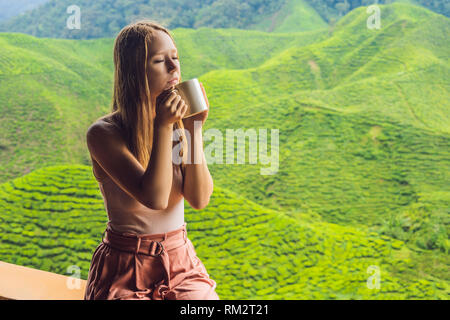 Giovane donna sana bere il tè verde contro una piantagione di tè. La sanità o la medicina di erbe concept Foto Stock