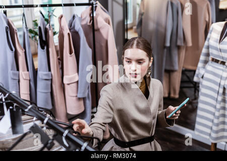 I giovani con i capelli lunghi donna graziosa con grandi orecchini in un elegante completo cercando gioiosa Foto Stock