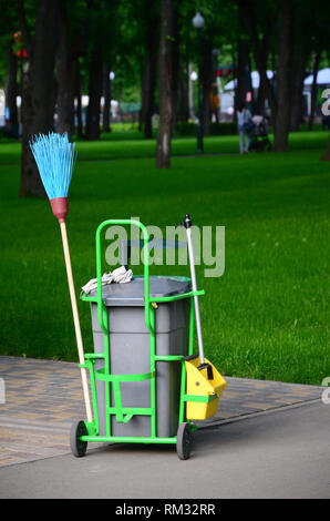 Il servizio di pulizia carrello pieno di forniture e attrezzature lungo con il grigio cestino per detergente professionale contro erba verde nel parco pubblico Foto Stock