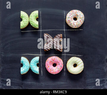 Tic Tac Toe fatta di ciambelle. Gioco una partita di tris con ciambelle sulla lavagna. Una dieta poco sana, il diabete, il concetto di zucchero. Vista superiore piatta o laici. Foto Stock