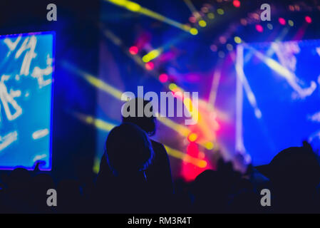 Silhouette di una grande folla al concerto contro una luminosa fase. Tempo di notte concerto rock con persone aventi fun il sollevamento in alto le mani in aria e Foto Stock