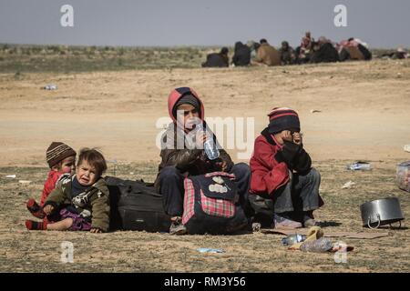 Deir Ezzor, Siria. 12 Feb, 2019. I bambini sono visto seduto con i loro beni come i civili fuggono lo Stato islamico-held villaggio di Baghouz nella parte orientale della provincia siriana di Deir Ezzor. Più di 1.500 persone hanno lasciato uno Stato islamico dell'ultima tasca nella parte orientale della Siria in passato 48 ore per fuggire alla battaglia tra i lottatori di siriano forze democratiche (SDF), un US-backed curdo led-gruppo di ribelli, e lo Stato islamico. Credito: Aboud Hamam/dpa/Alamy Live News Foto Stock