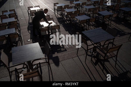 Stuttgart, Germania. Xiii Febbraio, 2019. Un dipendente di una caffetteria sulla Schlossplatz pulisce le tabelle dell'area all'aperto del ristorante. Credito: Marijan Murat/dpa/Alamy Live News Foto Stock