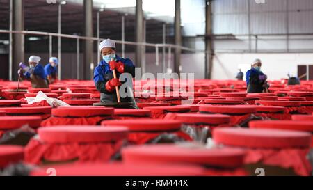 Qiandongnan, della Cina di Guizhou. Xiii Febbraio, 2019. Lavoratori agitare il rosso minestra acida in fermentazione ad un stabilimento di trasformazione alimentare in Majiang County, a sud-ovest della Cina di Guizhou, Feb 13, 2019. Rosso minestra acida, come una zuppa tradizionale in Qiandongnan Miao e Dong prefettura autonoma, è realizzato da i peperoncini freschi, pomodori e gingers. Credito: Cai Xingwen/Xinhua/Alamy Live News Foto Stock