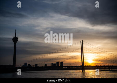 13 febbraio 2019, nella Renania settentrionale-Vestfalia, Düsseldorf: il sole tramonta dietro il ponte Rheinkniebrücke. Sul lato sinistro è possibile vedere la Torre sul Reno. Foto: Christophe Gateau/dpa Foto Stock