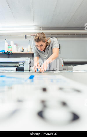 Donna segni di taglio o vinil avvolge la produzione di materiale pubblicitario in officina di agenzia Foto Stock