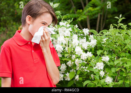 Ragazzo adolescente con influenza stagionale soffia il naso su un tessuto in un giardino di Primavera - stagione concetto di infezione Foto Stock