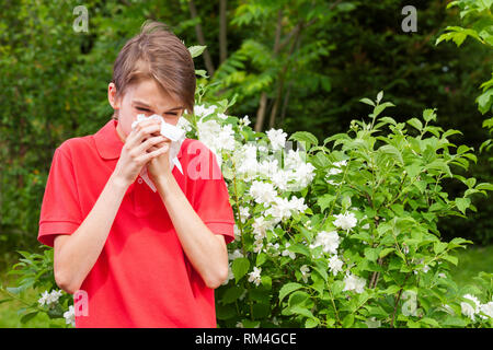 Ragazzo adolescente con influenza stagionale soffia il naso su un tessuto in un giardino di Primavera - stagione concetto di infezione Foto Stock