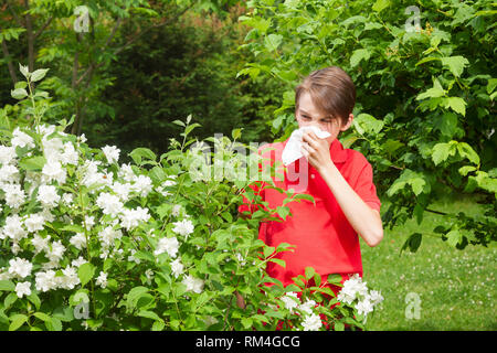 Ragazzo adolescente con influenza stagionale soffia il naso su un tessuto in un giardino di Primavera - stagione concetto di infezione Foto Stock