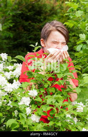 Ragazzo adolescente con influenza stagionale di starnuti ripetuti in un giardino di Primavera - stagione concetto di infezione Foto Stock