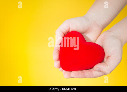 Cuore rosso sta tenendo in mano su giallo Foto Stock